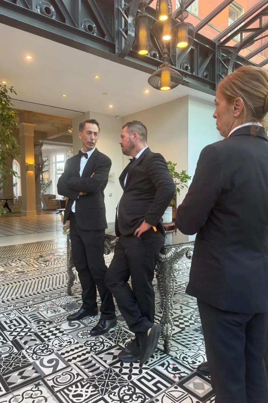 Trois personnes en costume discutent dans un hall élégant.